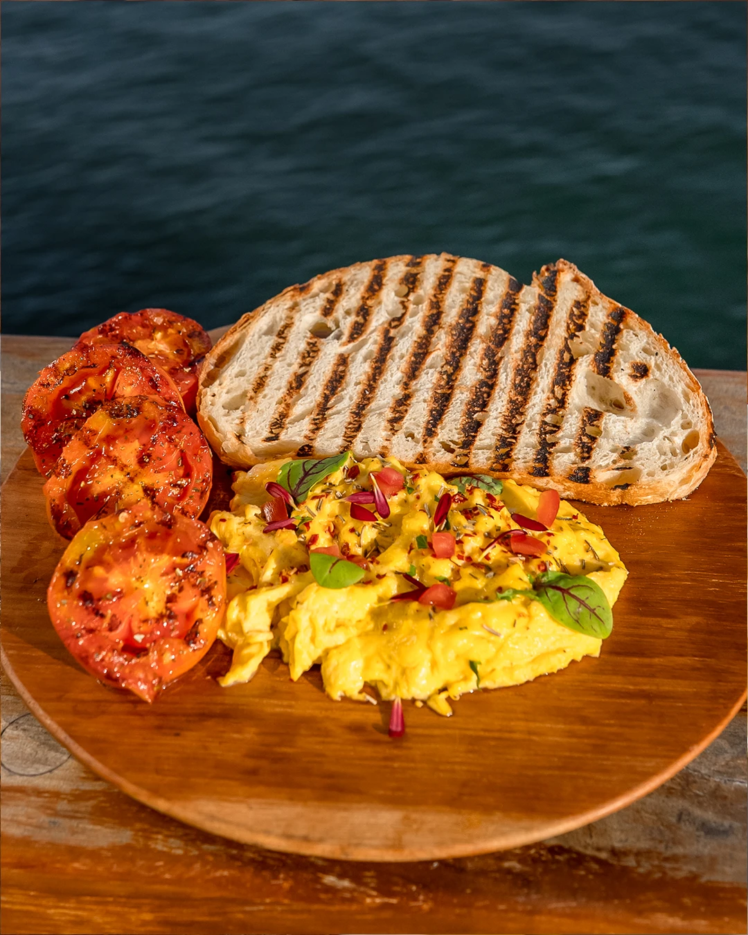 Grilled tomatoes and scrambled eggs served with slices of sourdough bread.