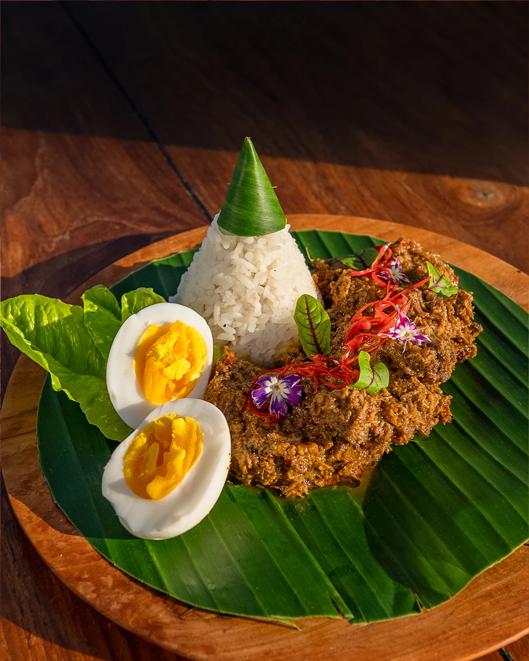 Traditional Indonesian rendang with rice and boiled eggs on a banana leaf.