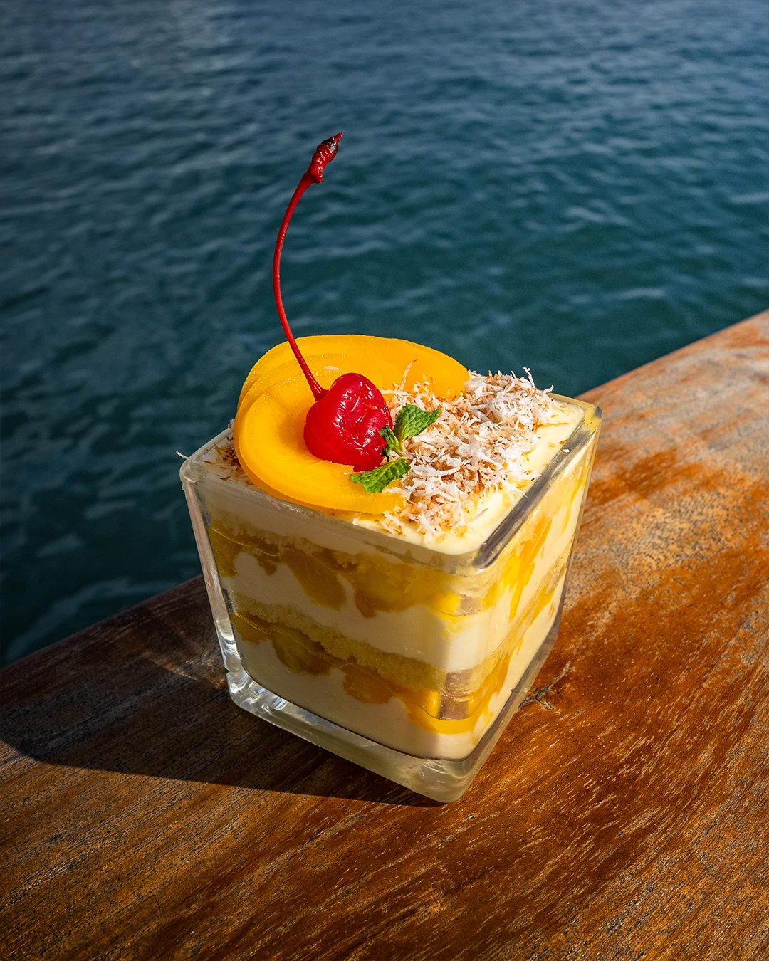 Layered mango trifle dessert in a glass topped with cherry and coconut.