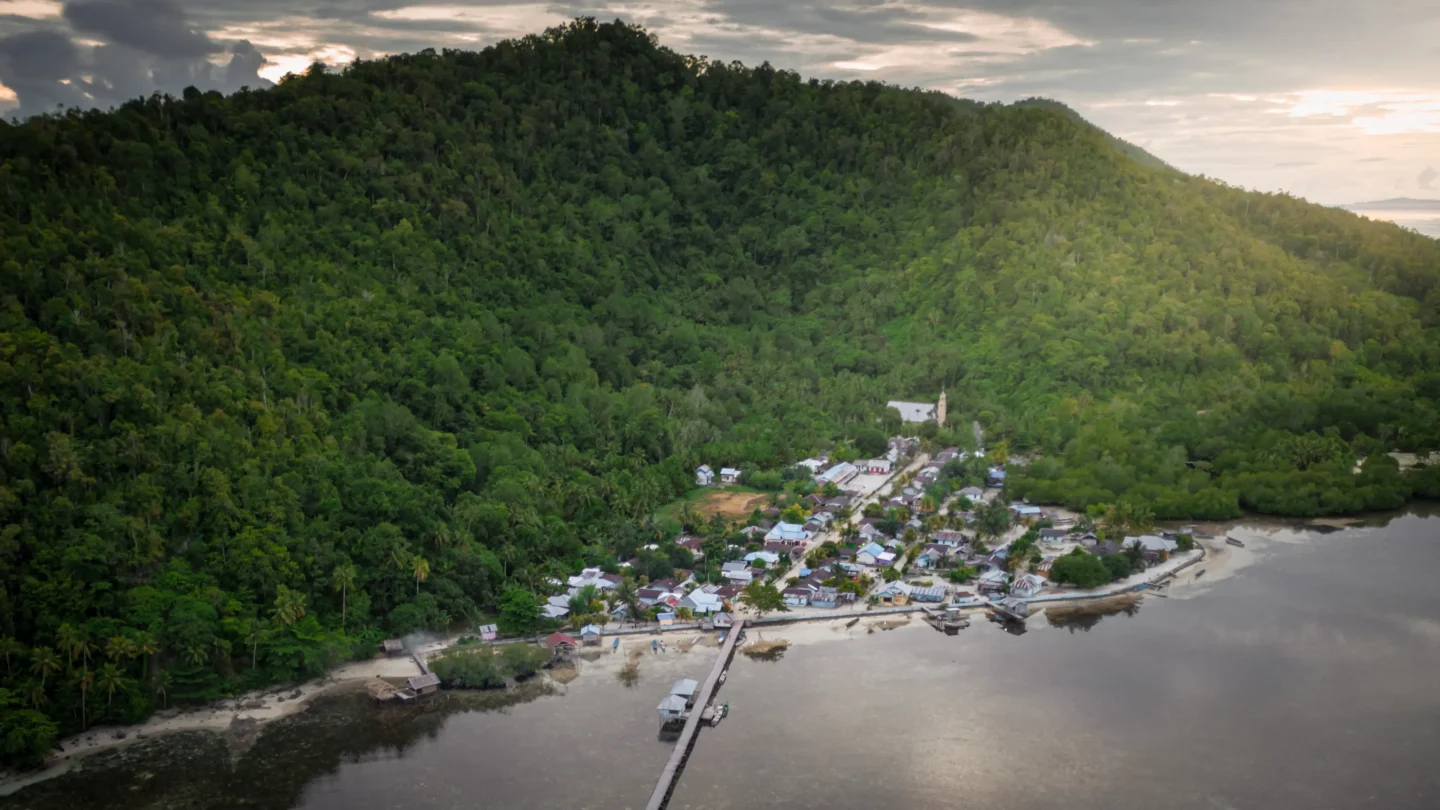 Yenbuba Village jetty on Mansuar Island with clear shallow water and coral reef below, a popular spot for snorkelling and night diving
